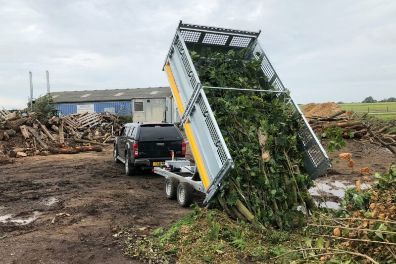 A Brian James trailer tipping tree cuttings onto a building site.